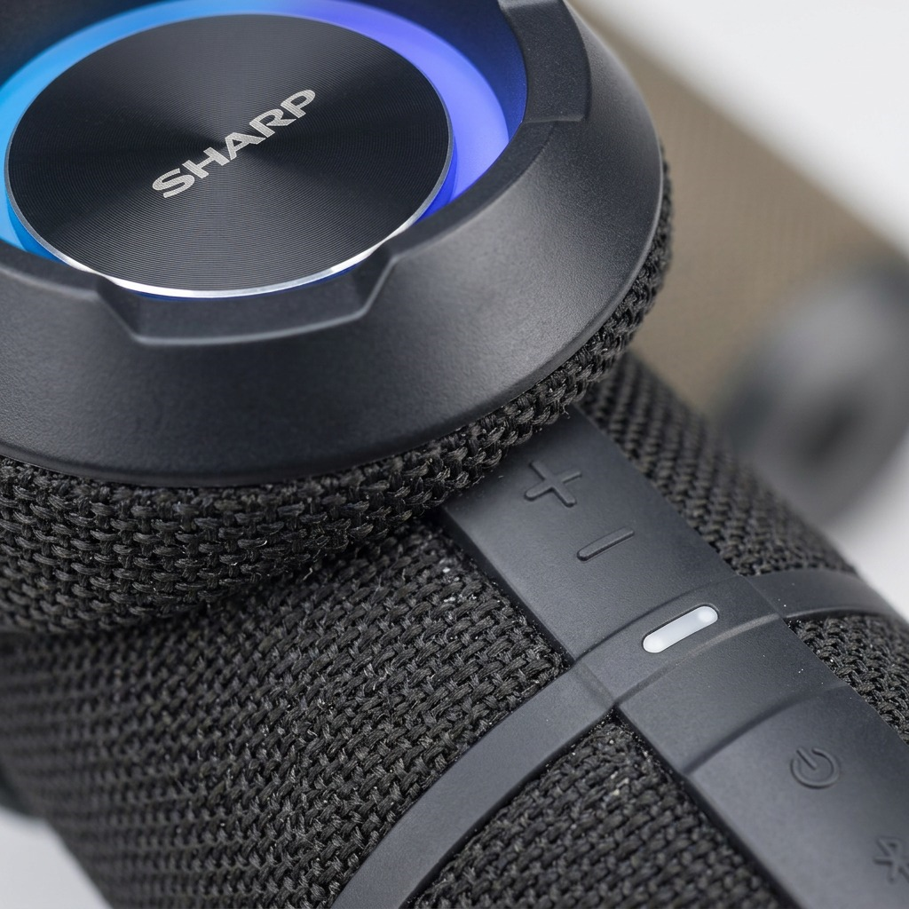 Macro detail of the SHARP GX-BT290-BK speaker, focusing on its top surface, woven grille, controls, and RGB ring.