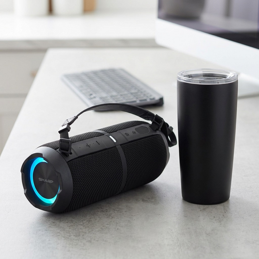 A photorealistic desk scene showing a SHARP GX-BT390 speaker beside a standard black travel tumbler for scale.