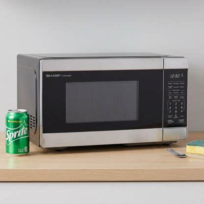 A photo of the Sharp Carousel microwave on a kitchen counter with a soda can, spoon, and sponge.