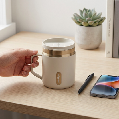 Hand holding a Contigo 14oz Snapseal Mug in Oatmilk on a desk next to a smartphone for scale.